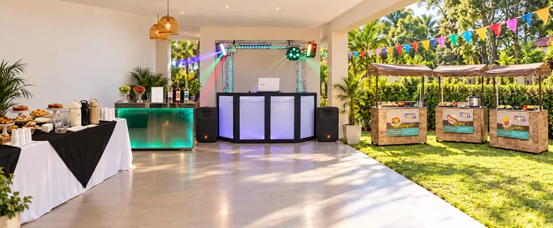 Espaço de evento com coffee break, bar com balcão iluminado, cabine de DJ e barraquinhas de lanches montados, sem pessoas (imagem ilustrativa).
